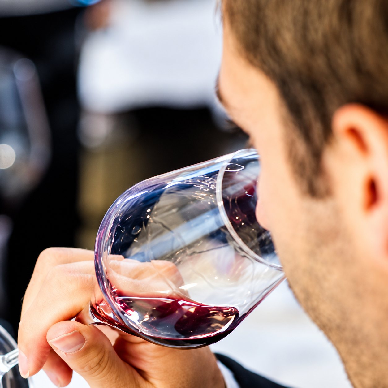 Un homme penche un verre à pied contenant un peu de vin rouge pour en sentir les arômes lors d'une dégustation.
