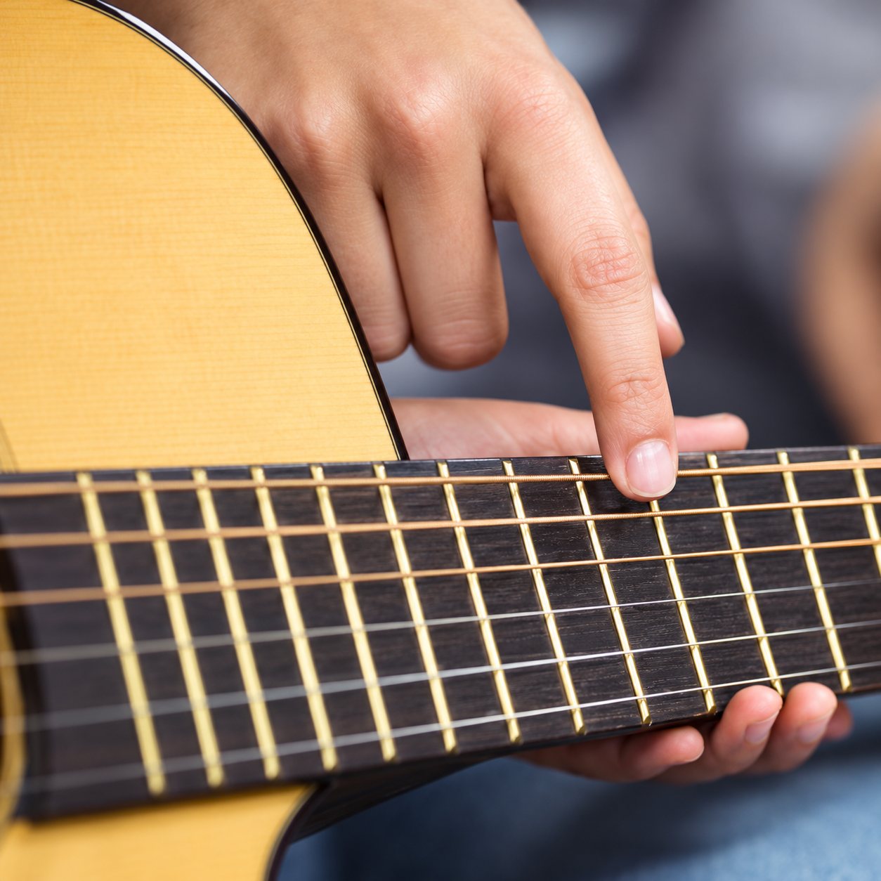 Gros plan sur une main qui appuie un doigt sur les frettes du manche d'une guitare classique en bois clair.